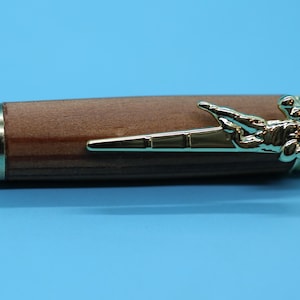 May include: A wooden pen with a gold-tone football player design on the end. The pen has a silver-tone band with numbers on it.