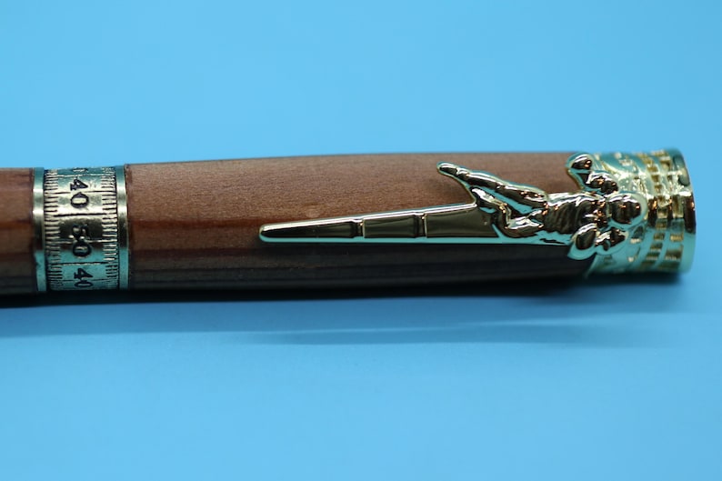 May include: A wooden pen with a gold-tone football player design on the end. The pen has a silver-tone band with numbers on it.