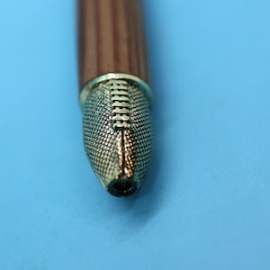 May include: Close-up of a brown wooden pen with a gold-colored tip. The tip has a textured design.