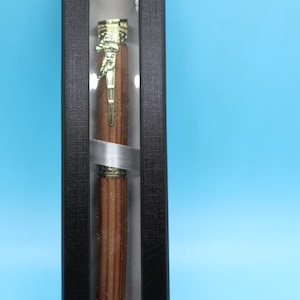May include: A wooden pen with a gold-colored top and a clear plastic display case. The pen is in a black box with a textured surface.