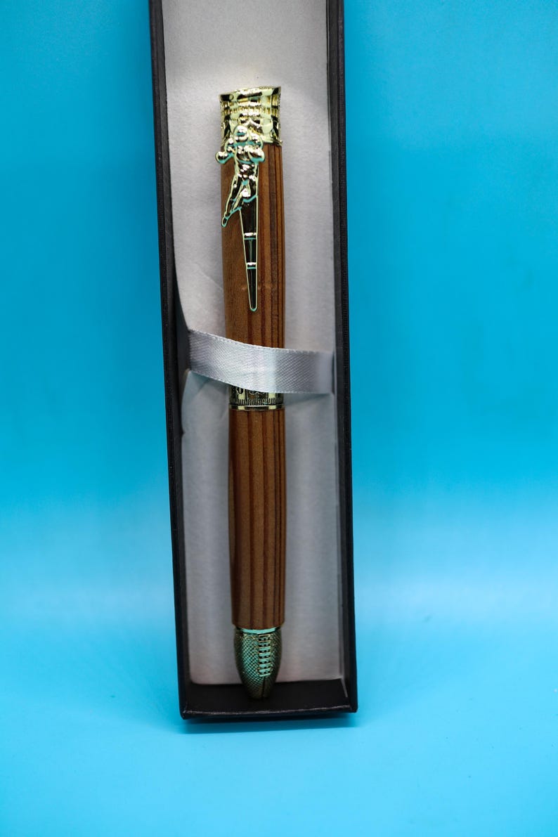 May include: A wooden pen with a gold-toned top and bottom. The pen is in a black box with a white ribbon.