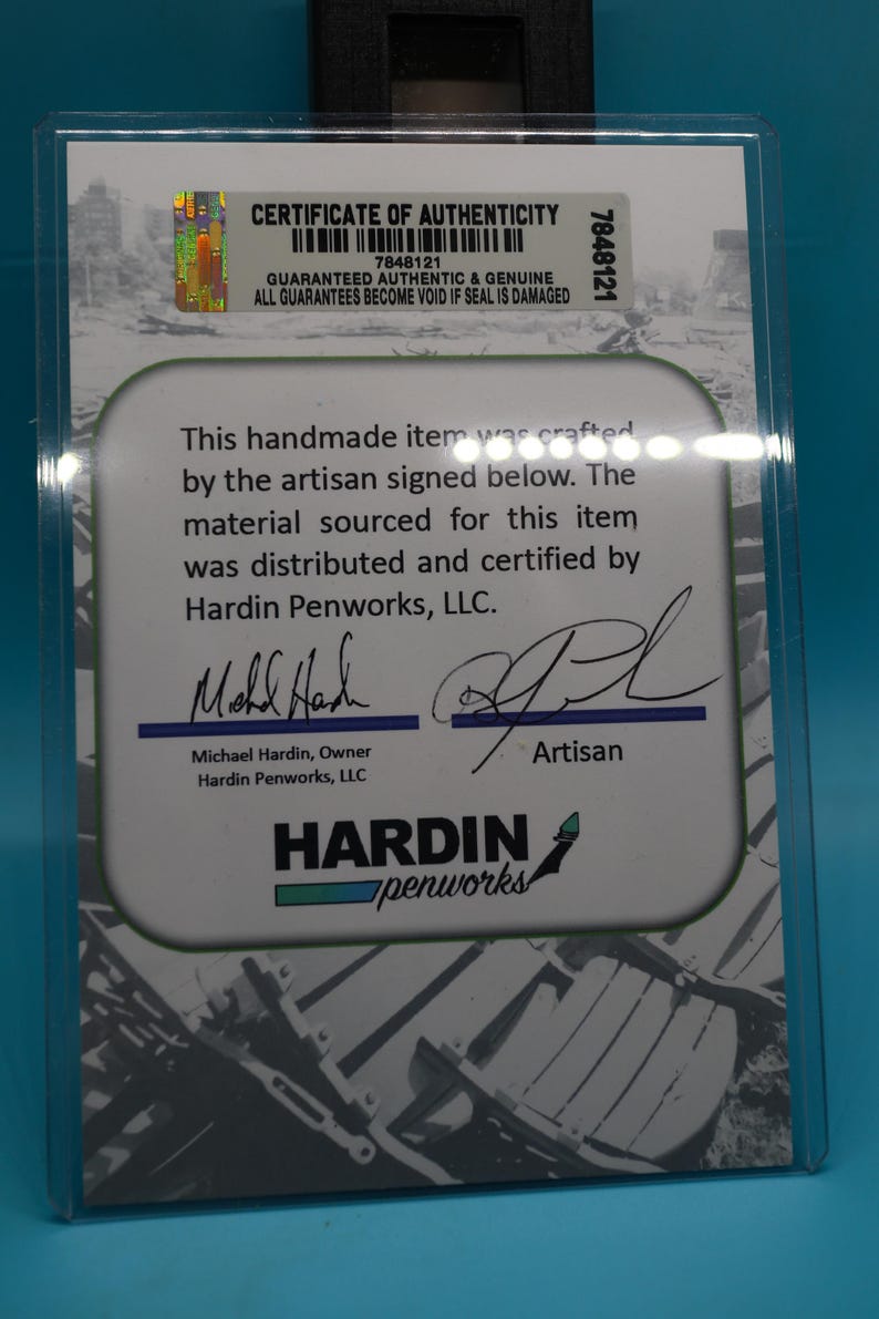 May include: Certificate of Authenticity for a handmade item. The certificate is white with black text and a black and white image of a chair. The text states that the item was crafted by the artisan signed below. The material sourced for this item was distributed and certified by Hardin Penworks, LLC. The certificate is signed by Michael Hardin, Owner of Hardin Penworks, LLC and the artisan.