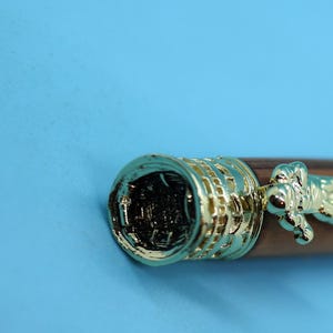 May include: Close-up of a brown wooden pen with gold accents. The pen has a detailed design on the cap and a gold-colored figure on the barrel.