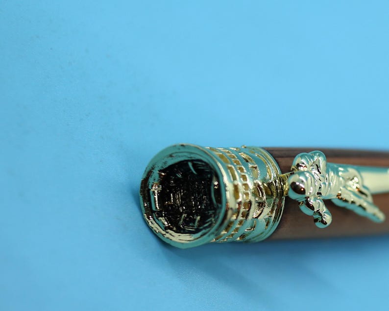 May include: Close-up of a brown wooden pen with gold accents. The pen has a detailed design on the cap and a gold-colored figure on the barrel.