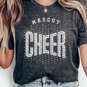 May include: A gray t-shirt with a white rhinestone design that says "MASCOT CHEER". The text "FONT INCLUDED for TEAM NAME" is at the bottom of the image.