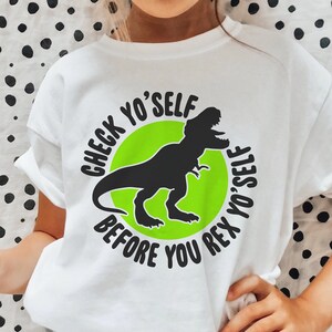 May include: A white t-shirt with a green circle and a black silhouette of a Tyrannosaurus Rex. The text "CHECK YO'SELF BEFORE YOU REX YO'SELF" is written around the circle.