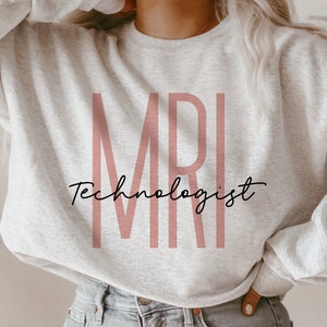 Puede incluir: Una sudadera gris con el texto "MRI Technologist" en letras rosas.
