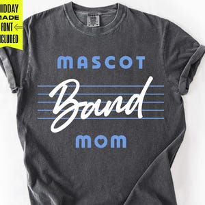 Könnte beinhalten: Dunkelgraues T-Shirt mit den Wörtern "MASCOT Band MOM" in blauer und weißer Schrift. Das Wort "Band" ist in Schreibschrift gehalten. Das Shirt hat einen Vintage-Look.