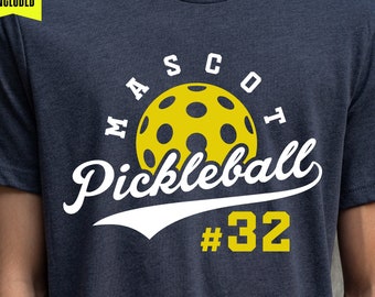 Könnte beinhalten: Ein dunkelblaues T-Shirt mit einem weißen Design, auf dem "MASCOT Pickleball #32" steht. Das Design enthält einen gelben Pickleball mit schwarzen Löchern.