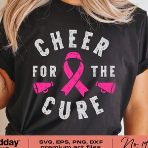 Puede incluir: Una camiseta negra con un diseño gráfico blanco que dice "Cheer for the Cure" con una cinta rosa en el centro. El gráfico tiene un aspecto desgastado.