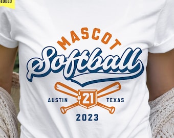 May include: A white t-shirt with a blue and orange design that says "MASCOT Softball" with crossed baseball bats and the text "AUSTIN #21 TEXAS 2023".