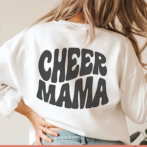 May include: White sweatshirt with black text that reads "CHEER MAMA" in a retro font style. The text is centred on the back of the sweatshirt.