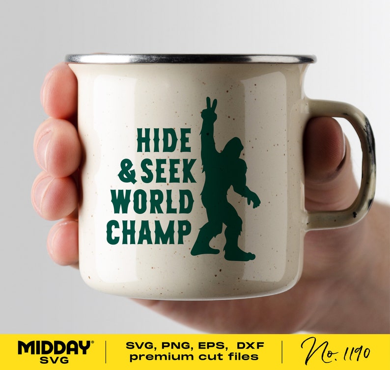 May include: A white enamel mug with a green silhouette of Bigfoot giving the peace sign. The text "HIDE & SEEK WORLD CHAMP" is printed in green on the mug.