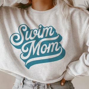 May include: A gray sweatshirt with the text "Swim Mom" in a blue retro font.