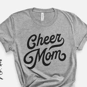 Puede incluir: Camiseta gris con texto negro que dice "Cheer Mom" en una fuente retro.