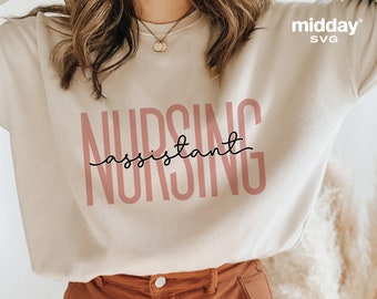 Puede incluir: Una sudadera blanca con el texto "Nursing assistant" impreso en rosa y negro. El texto está en una fuente en negrita y estilizada.