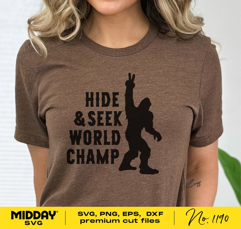 May include: A brown t-shirt with a black silhouette of a Bigfoot raising its hand in a peace sign. The text "HIDE & SEEK WORLD CHAMP" is printed on the shirt.