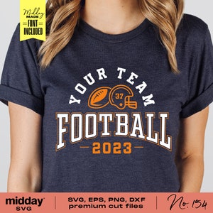 May include: A navy blue t-shirt with an orange and white design that says "Your Team Football 2023". The design includes a football and a helmet.