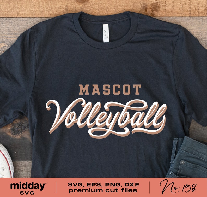 以下が含まれることがあります： 「MASCOT Volleyball」と書いてある、茶色と白のデザインの黒いTシャツです。