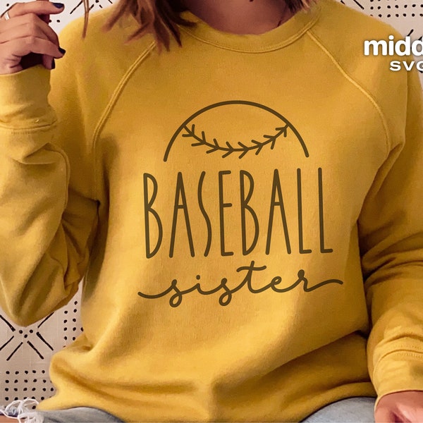 May include: Mustard yellow sweatshirt with the words "Baseball Sister" in a dark brown font. The word "Baseball" is above the word "sister" and is partially enclosed by a baseball design. The sweatshirt has long sleeves.