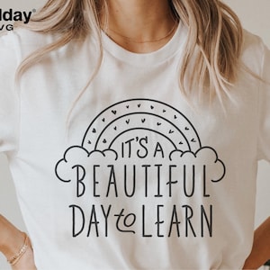 May include: White t-shirt with a black graphic design of a rainbow with hearts and the text "It's a beautiful day to learn."