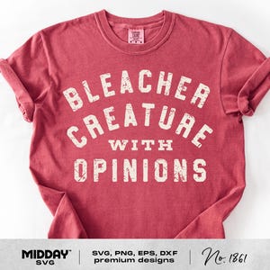 May include: A red t-shirt with the text "BLEACHER CREATURE WITH OPINIONS" in a distressed, off-white font. The shirt has a crew neck and rolled-up sleeves. The bottom of the shirt has the text "MIDDAY SVG" and "No. 1861".