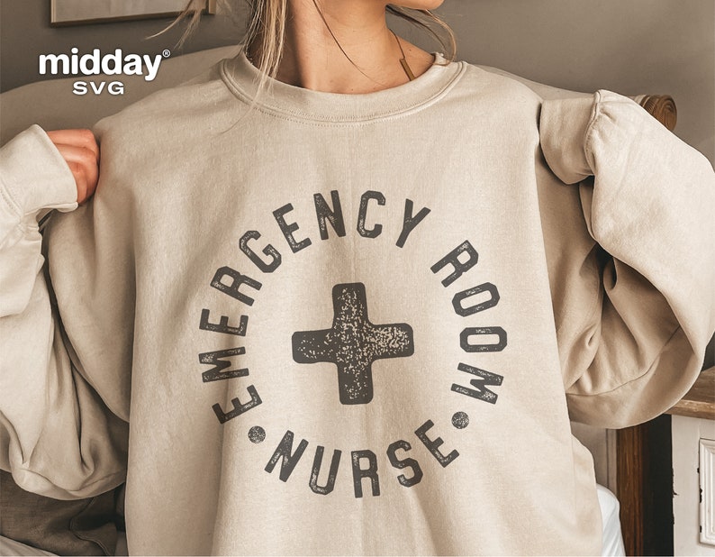 Peut inclure: Un sweat-shirt beige avec un imprim&eacute; graphique noir qui dit "Emergency Room Nurse" dans un cercle avec un signe plus noir au centre.
