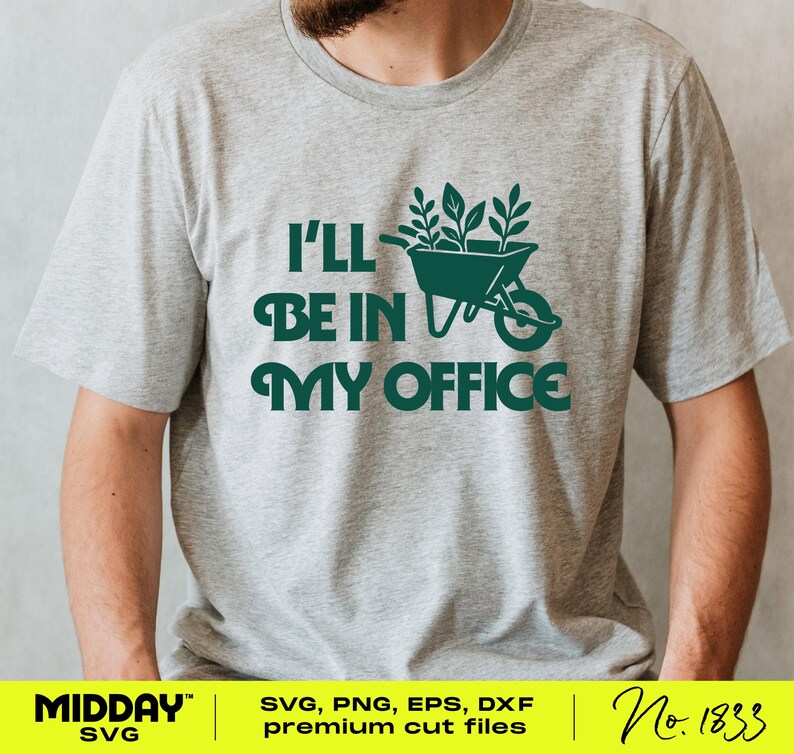 May include: A light grey t-shirt featuring the text "I'LL BE IN MY OFFICE" in dark green. The design includes a wheelbarrow filled with plants. This is a casual wear item.