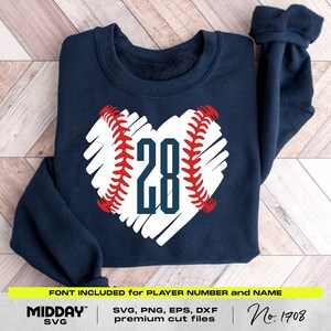 May include: A navy blue sweatshirt with a white heart-shaped baseball design. The baseball has red stitching and the number "28" in the center. The text "FONT INCLUDED for PLAYER NUMBER and NAME" is at the bottom of the image. The text "MIDDAY SVG" is in the lower left corner. The text "SVG, PNG, EPS, DXF premium cut files" is in the lower center. The text "No. 1708" is in the lower right corner.