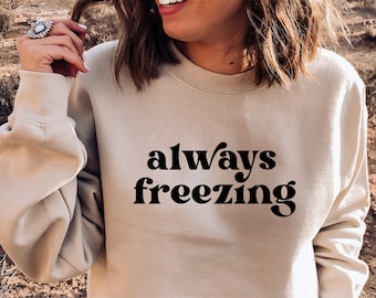以下が含まれることがあります： ベージュのトレーナーに、黒いレトロな文字で「always freezing」と書かれています。