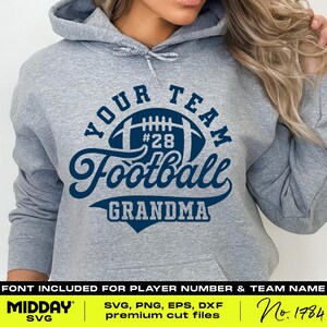 Pu&ograve; includere: Felpa grigia con un design blu e bianco che dice "Your Team Football Grandma". Il design include un pallone da calcio con il numero 28.