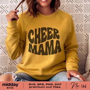 May include: A yellow sweatshirt with the text "CHEER MAMA" in brown, retro-style lettering.