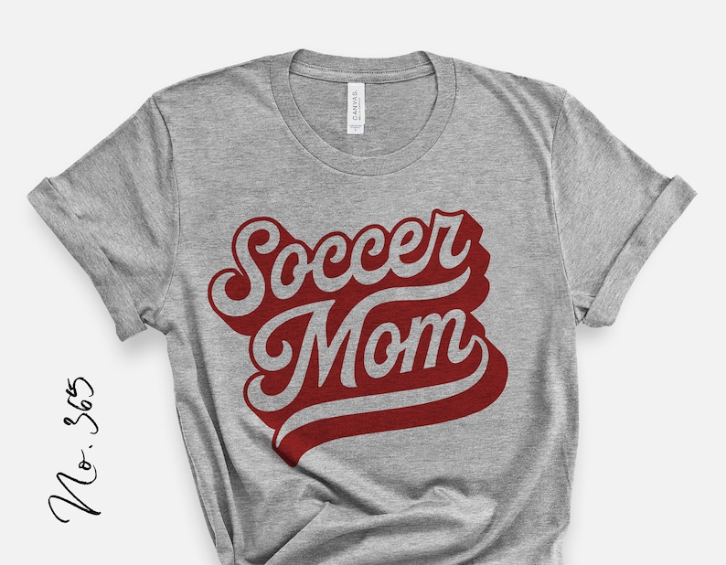 K&ouml;nnte beinhalten: Graues T-Shirt mit dem Text "Soccer Mom" in roten und wei&szlig;en Buchstaben.