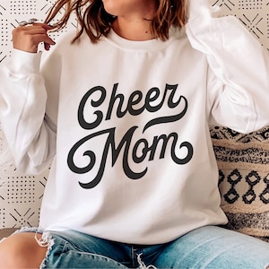 Puede incluir: Sudadera blanca con texto negro que dice "Cheer Mom" en una fuente retro.