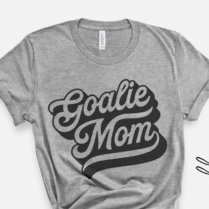 May include: Gray t-shirt with the text "Goalie Mom" in a retro, black, stylized font.