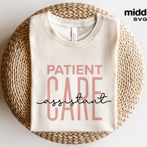 May include: A beige t-shirt with the text "PATIENT CARE assistant" in pink and black lettering.