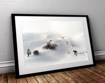 May include: A black and white photograph of a ski lift ascending a snow-covered mountain. The lift is empty and the mountain is covered in a thick layer of snow. The sky is overcast and the air is still.