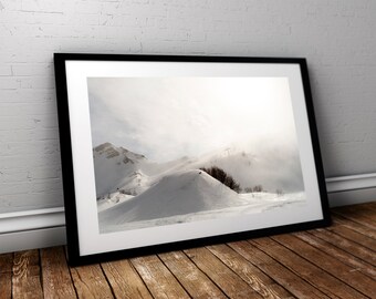 May include: A framed photograph of a snowy mountain landscape. The mountains are covered in white snow and the sky is a light blue with some clouds. The sun is shining brightly and there is a faint mist in the air.