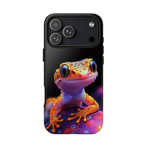 May include: A black smartphone case featuring a vibrant, high-contrast illustration of a gecko with large, dark eyes and orange, yellow, and blue spotted skin. The gecko is positioned on a textured, colorful surface against a dark background.