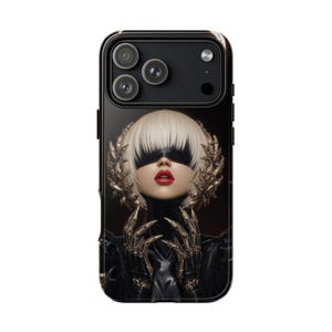 May include: Black phone case featuring a digital art portrait of a person with white hair, a blindfold, and red lipstick. The person is wearing a black outfit with gold-colored, ornate hand-like structures.
