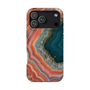 May include: A smartphone case featuring a vibrant agate stone pattern with concentric bands of orange, coral, and deep teal. The design includes a crystalline center with gold-toned accents and a black camera module cutout at the top.