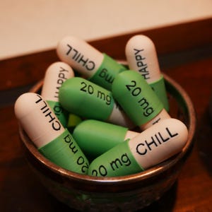 May include: A bowl filled with green and white capsules. The capsules are labeled with the words "CHILL" and "HAPPY" and the dosage "20 mg".