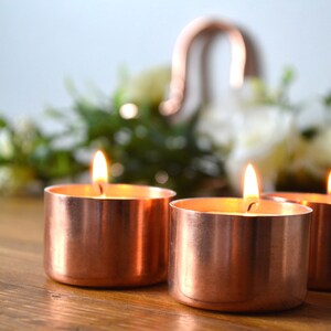 May include: Three copper candle holders with lit tea lights on a wooden surface.