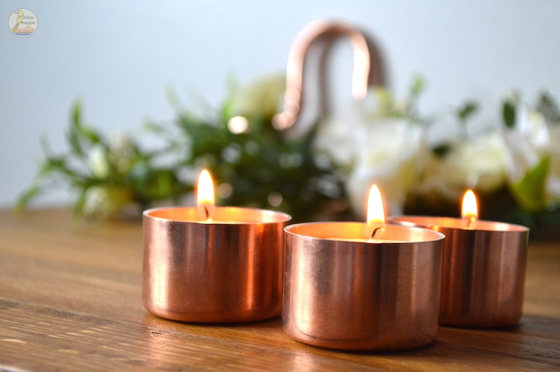 May include: Three copper candle holders with lit tea lights on a wooden surface.