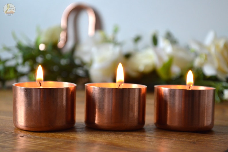 May include: Three copper candle holders with tea lights burning inside. The candle holders are on a wooden surface.