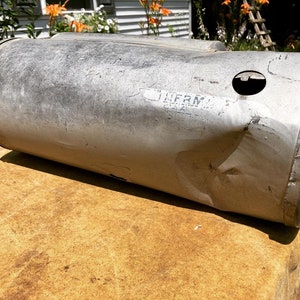 Op de afbeelding: Een zilveren metalen cilinder met een deuk en een klein gat aan de zijkant. De cilinder heeft de tekst "LURM" erop.