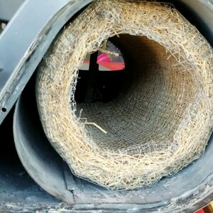 Op de afbeelding: Close-up van een ronde, grijze metalen buis met een stroomachtig materiaal eromheen gewikkeld. Het stroomachtige materiaal wordt op zijn plaats gehouden door een draadgaas.