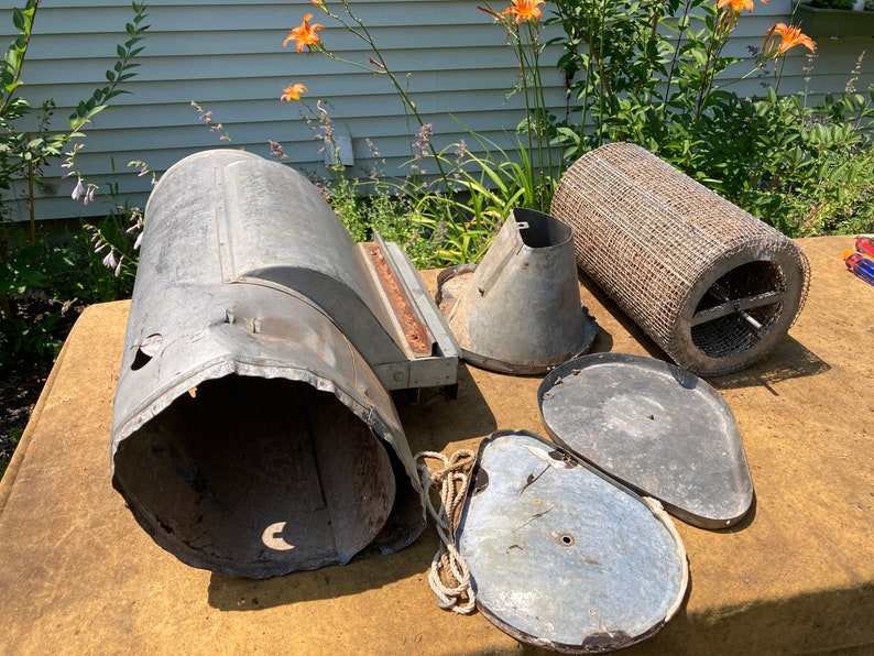 Op de afbeelding: Een set vintage metalen onderdelen voor een vogelvoeder. De set bevat een grote cilindrische basis, een trechter, twee deksels en een draadgaascilinder.