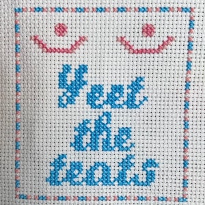 Puede incluir: Bordado de punto de cruz con un borde azul y rosa. El bordado dice "Keep on smiling" con una carita sonriente rosa encima del texto.