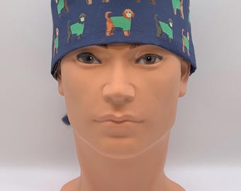 May include: A navy blue surgical scrub cap featuring a repeating pattern of brown dogs wearing green sweaters and face masks. The cap is tied at the back and is designed for medical professionals or pet lovers.